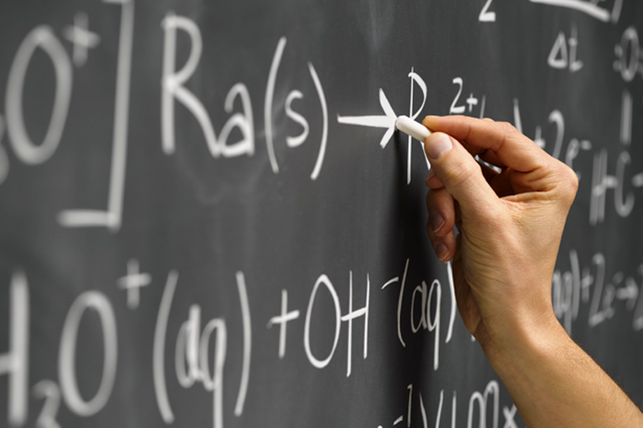 A hand writing mathematical equations on a blackboard with white chalk.