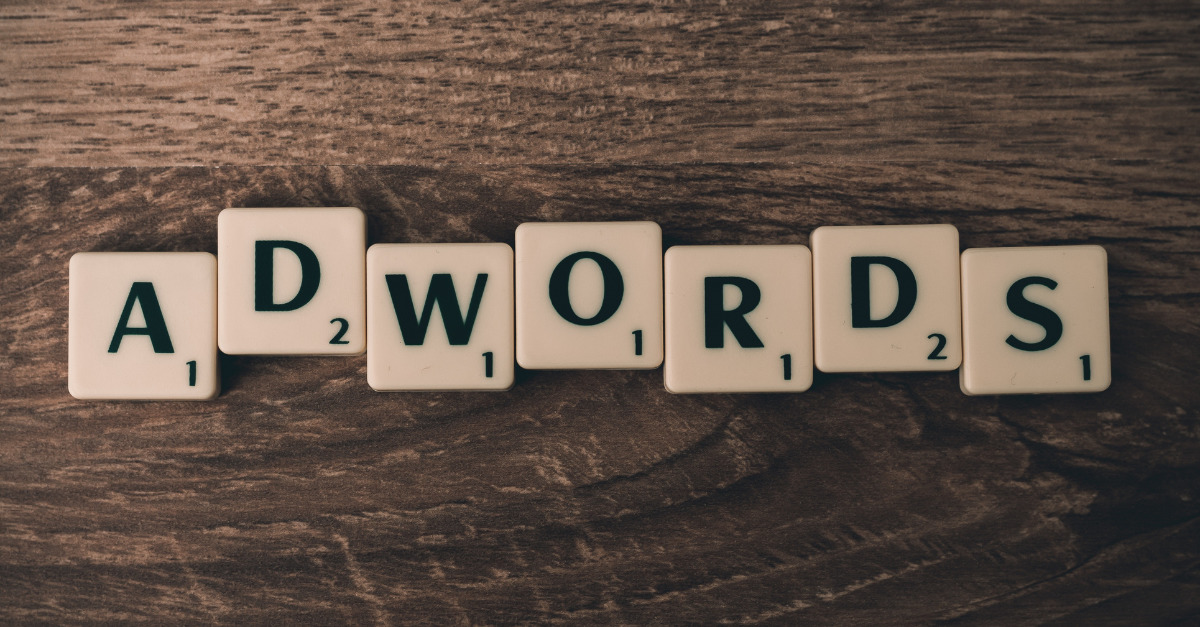 Scrabble tiles spell out "ADWORDS" on a wooden surface.
