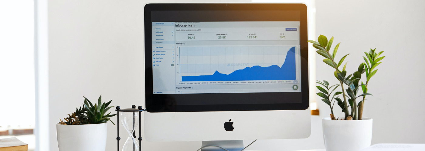 A computer monitor displays a rising line graph with analytics data, flanked by potted plants on a bright desk.