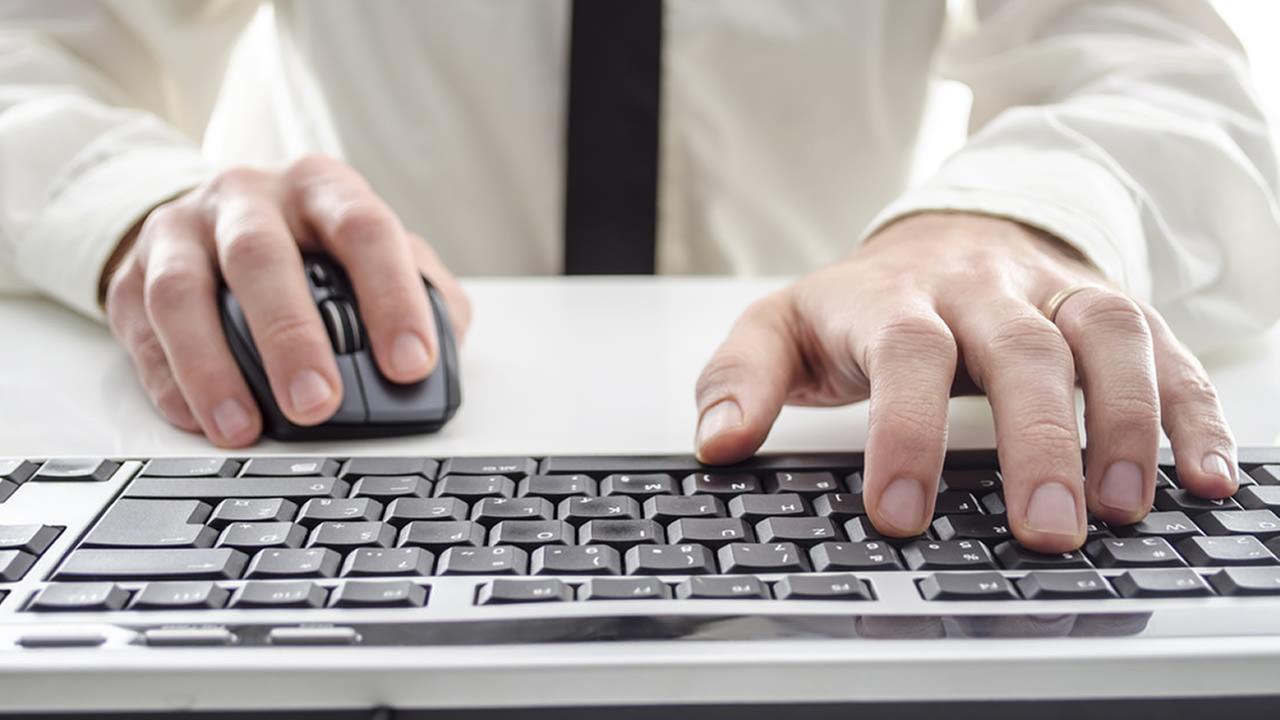 A person in a white shirt uses a computer mouse with one hand and types on a keyboard with the other.